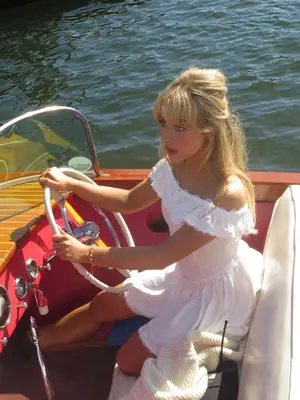 Sabrina Carpenter wears a white off-shoulder mini dress while driving a boat