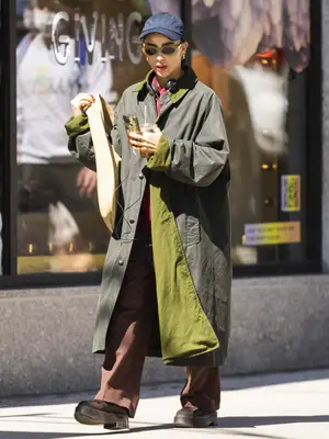 Zoe Kravitz wears a green jacket, navy baseball cap, oval sunglasses, wide-leg pants, and platform boots