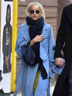 Zoe Kravitz wears a blue suede coat, scarf, sunglasses, silk bag, and olive pants