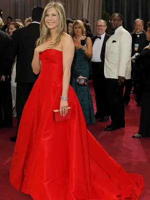 Jennifer Aniston wears a red strapless Valentino gown, hard-sided clutch, and layered bracelets to the 2013 Oscars 