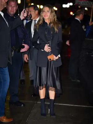Jennifer Aniston wears a black slip dress, blazer, and heeled boots