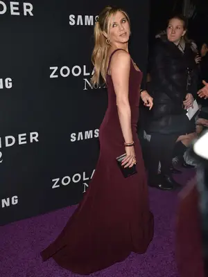 Jennifer Aniston wears a wine-toned Galvan gown, black clutch, and gold jewelry to the Zoolander No.2 premiere
