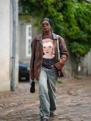 Woman walking with graphic sweater, leather tailored jacket, baggy jeans, shield sunglasses, and hair wrap