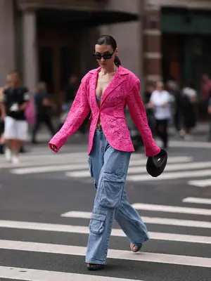 Woman wearing pink crochet blazer, cargo jeans, open-toed shoes, black handbag, and sunglasses