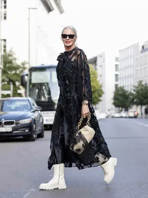 Petra van Bremen wears a sheer floral maxi dress, chunky white lace-up boots, sunglasses, and a tan handbag
