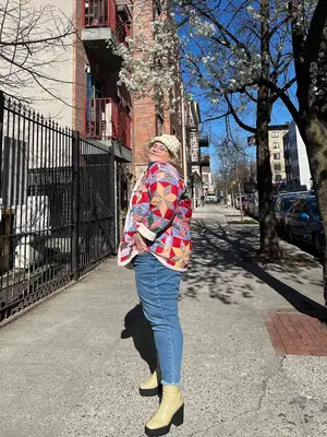 Abby Bible wears a patchwork coat, jeans, cream boots with chunky black soles, and houndstooth bucket hat