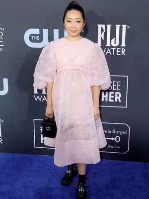 Lulu Wang wears a pink puff-sleeved dress, black structured handbag, and black chunky boots with gold detailing