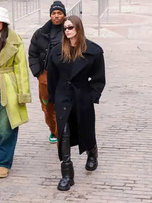 Hailey Bieber wears a structured black coat, skinny rectangle sunglasses, chunky black puffer boots, and leather pants