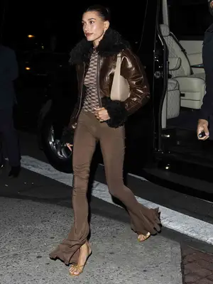 Hailey Bieber wears a brown fur-trim jacket, patterned top, flare pants, and purse in New York City