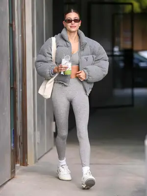 Hailey Bieber wears a gray Prada puffer coat, sports bra, leggings, and white sneakers in Los Angeles