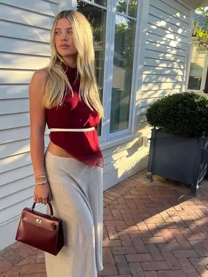 Sofia Richie Grainge wearing a red tank top, gray maxi skirt, white belt, and bordeaux handbag