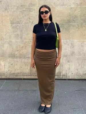 Jill Kortleve wearing a brown skirt, black cropped tee, black glove flats, lime green handbag, sunglasses, and layered necklaces