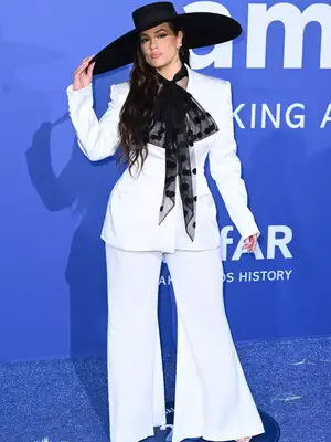 Ashley Graham wears a white Nina Ricci suit with sheer dotted pussy bow and wide-brim hat to the 2023 amfAR Cannes Gala