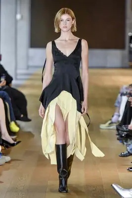 Model wearing black dress with butter yellow streamer fringe and black boots at the Monse Spring 2025 show