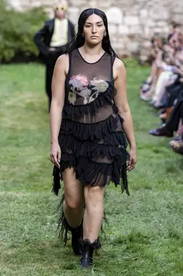 Yumi Nu wears a tiered ruffled sheer black mini dress and frilly boots at the Collina Strada Spring 2025 show