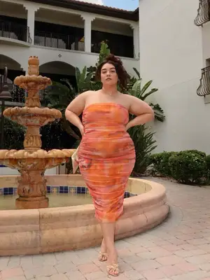 Influencer @nadiaaboulhosn is standing outside wearing a orange tube dress with tan sandals 