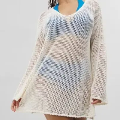 A model is wearing a white crochet long-sleeve cover up over a blue bikini 