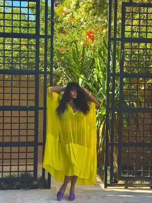 Model Precious Lee is standing outside wearing a yellow-green kaftan over a bikini and purple slides 