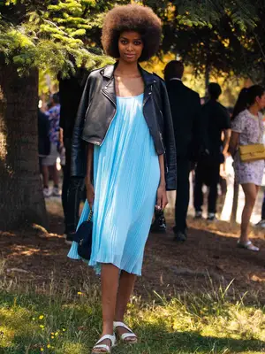 Model Blesnya Minher wears a short black leather jacket on her shoulders, baby blue long cami swing summer dress, and white sandals 