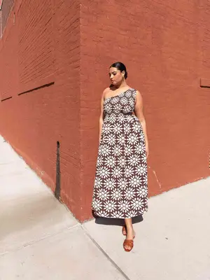 Model wearing a one-shoulder brown and white nap dress with tan, open-toe shoes and low bun hairstyle