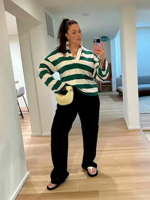 Ashley Graham wears a green and white striped rugby shirt, black loose pants, and knotted Bottega Veneta bag