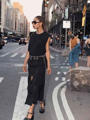 Content creator Opal wears a black sleeveless dress, body chains with charms, aviator sunglasses, and strappy sandals