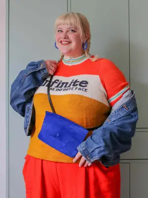 Content creator Lydia Morrow wears a color block graphic sweater, denim jacket, and blue accessories