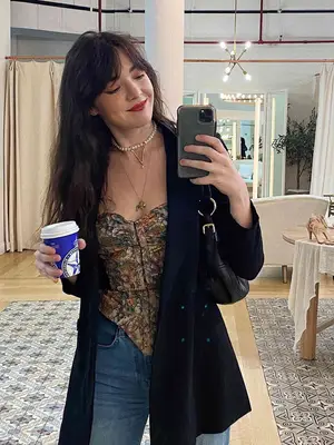 MYM Beauty editor Madeline Hirsch wears a floral corset top, black jacket, shoulder bag, and layered necklaces