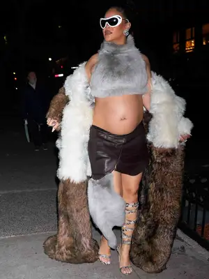 Rihanna wearing large white sunglasses, gray fur crop top, two-tone fur coat, leather mini skirt, and snakeskin gladiator sandals