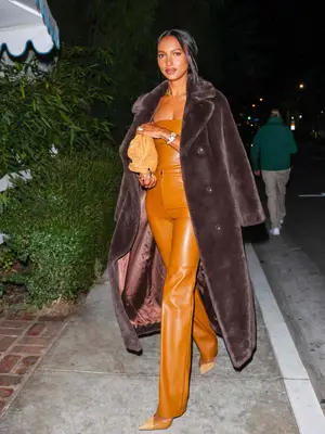 Jasmine Tookes wearing a brown fur trench coat, camel leather strapless top, leather pants, pointed-toe heels, and handbag