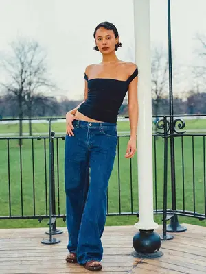 Alisha Boe wears black top, blue wide leg flared jeans, and brown boots