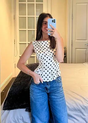 Person in a polka dot tank top and jeans taking a mirror selfie