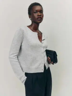 Woman wearing gray Reformation sweater, black trousers, and clutch