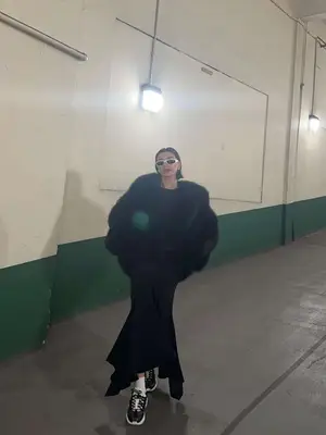 Hailey Bieber wearing a black coat, dress, sneakers, and white rectangular sunglasses