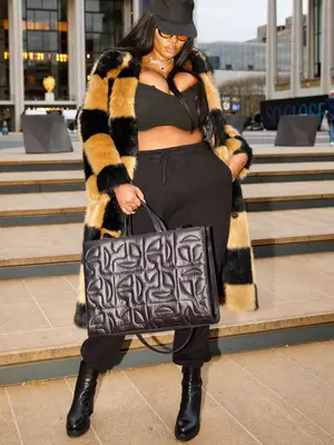 Precious Lee wears a black bra top, sweatpants, leather boots, puffer Telfar bag, checked coat, baseball cap, and sunglasses