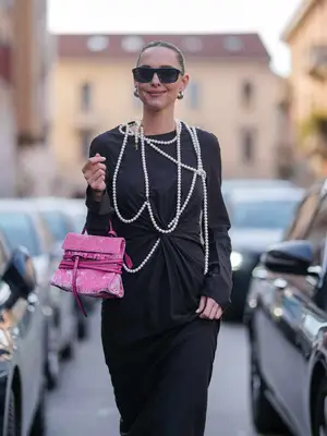 Woman wearing criss-cross layered pearls over black dress paired with sunglasses and pink handbag