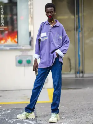 Woman with red curly hair in an all-black outfit with metallic silver Adidas sneakers