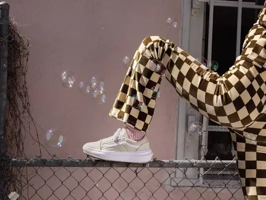 Close-up of person wearing beige Vans sneakers and brown and beige checkered jumpsuit
