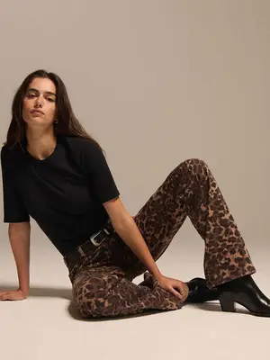 Model wearing leopard print pants with black belt and silver buckle, black tee, and black boots