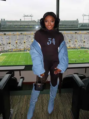 Simone Biles wearing black furry earmuffs, blue jacket, 34 shirt, and blue cowboy boots