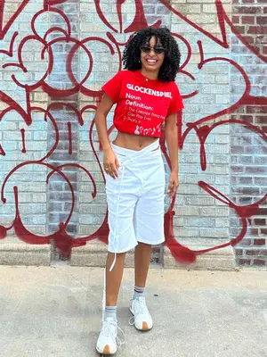 Yara Shahidi wearing red graphic tee, white shorts, sneakers, socks, and sunglasses