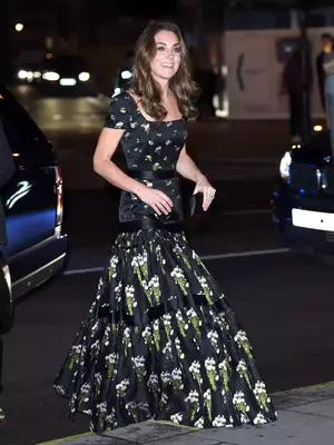 Kate Middleton arriving at a gala wearing a black floral gown and carrying a black clutch