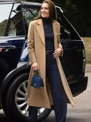 Kate Middleton wearing a black top and pants with a camel wool coat and a black bag