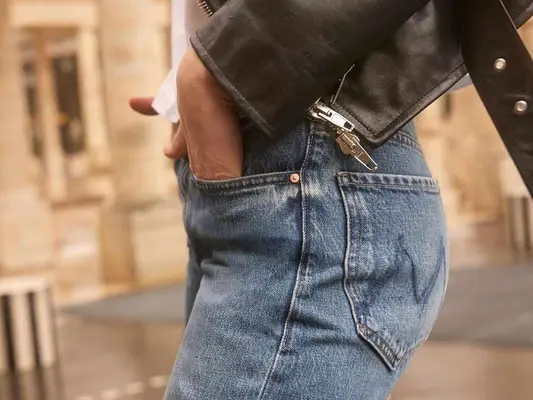 A person wearing jeans and a leather jacket, standing outdoors with one hand in their pocket