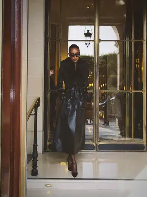 Jasmine Tookes wears a leather longline coat with fur trim, sunglasses, and strappy heels