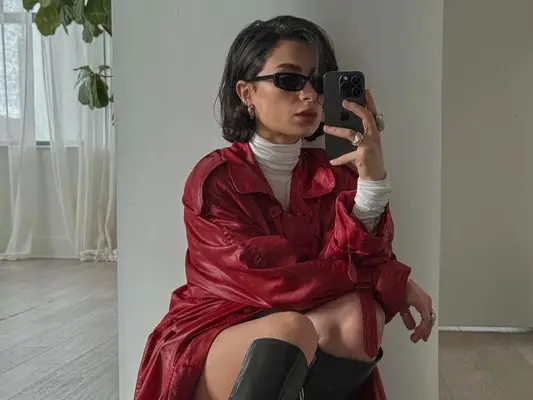Woman wearing red leather longline coat, black boots, white turtleneck, and black sunglasses