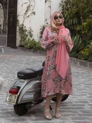Jennifer Coolidge wearing a pink printed caftan and pink scarf in The White Lotus