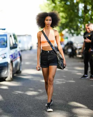 Woman wearing a cropped peach halter top with high-waisted black denim shorts and black Chuck Taylors