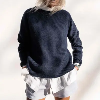 Close-up of woman wearing white button-down shirt, navy sweater, and striped shorts