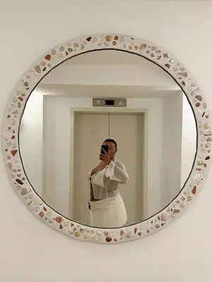 Paloma Elsesser takes a mirror selfie wearing sheer white blouse, white bikini top, and skirt